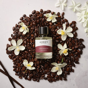 Joe Smooth perfume bottle on a bed of coffee beans surrounded by vanilla flowers
