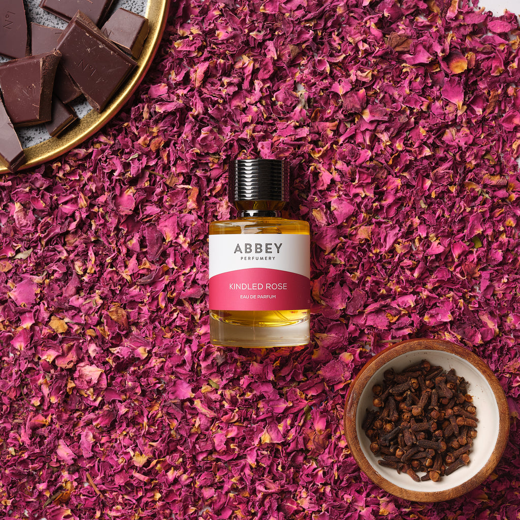 Kindled Rose perfume bottle on a bed of rose petals with a bowl of dark chocolate