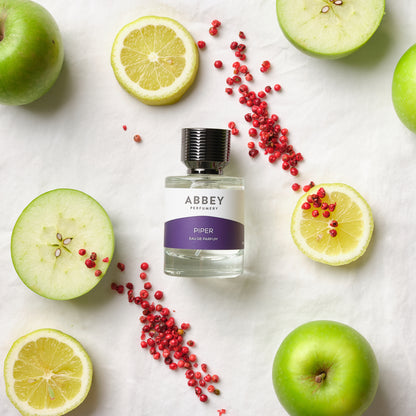 Piper perfume bottle surrounded by pink pepper with freshly cut apples and lemons